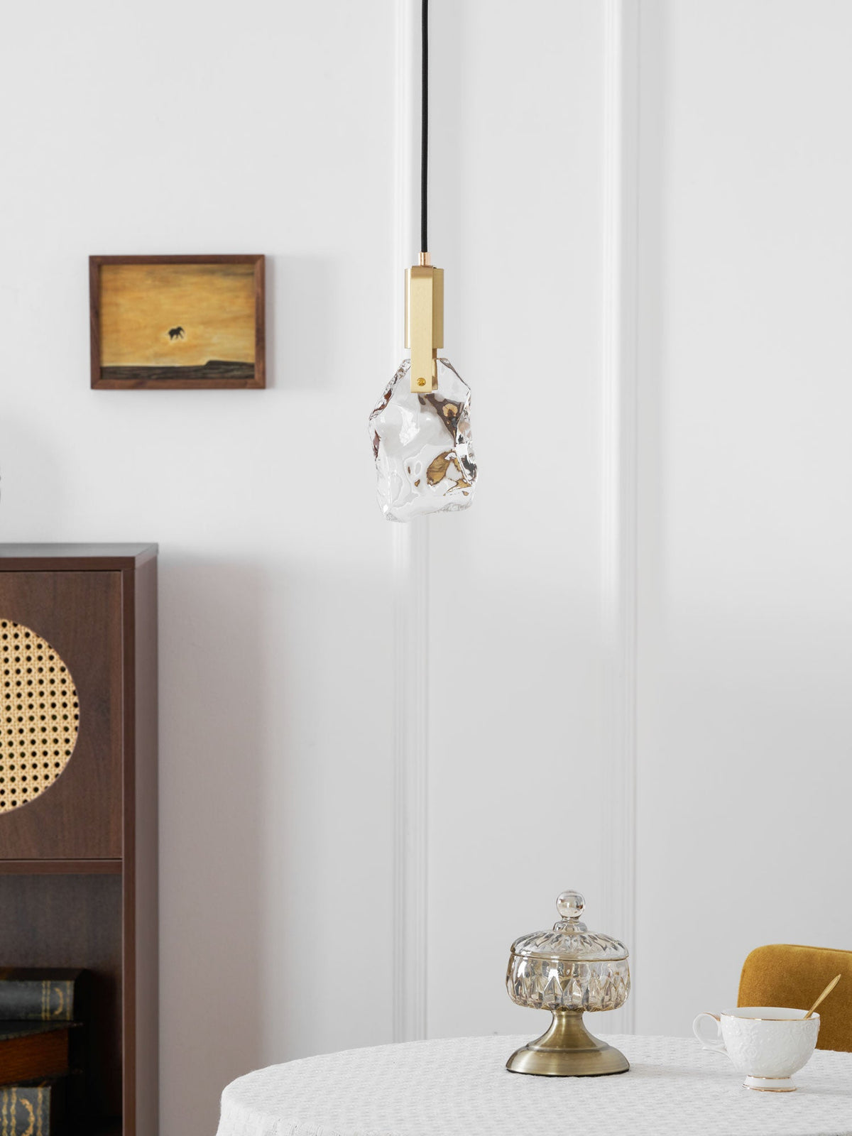 A slightly smaller view of the rock-glass Clérachic pendant by a white wall, a framed painting and a wooden cabinet.