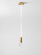 A single Clérachic pendant with a rock-like clear glass piece hangs from a brass ceiling canopy against a pale grey wall.