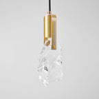 A closer view of the clear, rough-cut glass and brass bracket on this Clérachic pendant, with a faint glow at the top.