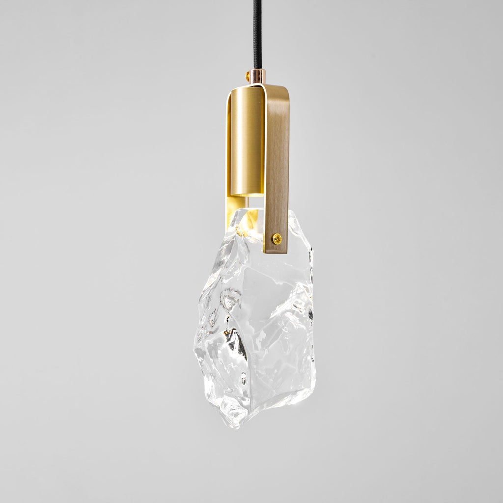 The rock-glass Clérachic pendant, seen from a lower angle, with its brass bracket and a warm glow under the cap.