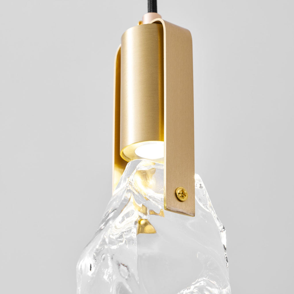 Close view of the brushed brass bracket and screw on this Clérachic pendant, with the bulb glowing at the top of the glass.