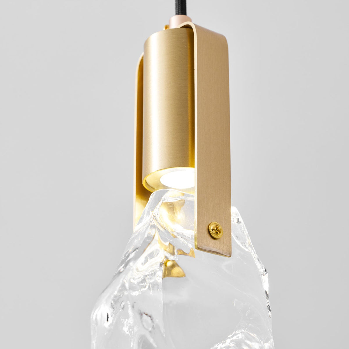 Close view of the brushed brass bracket and screw on this Clérachic pendant, with the bulb glowing at the top of the glass.