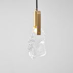 A front view of the rock-glass Clérachic pendant, with a brass bracket and a warm light at its top, on a pale backdrop.