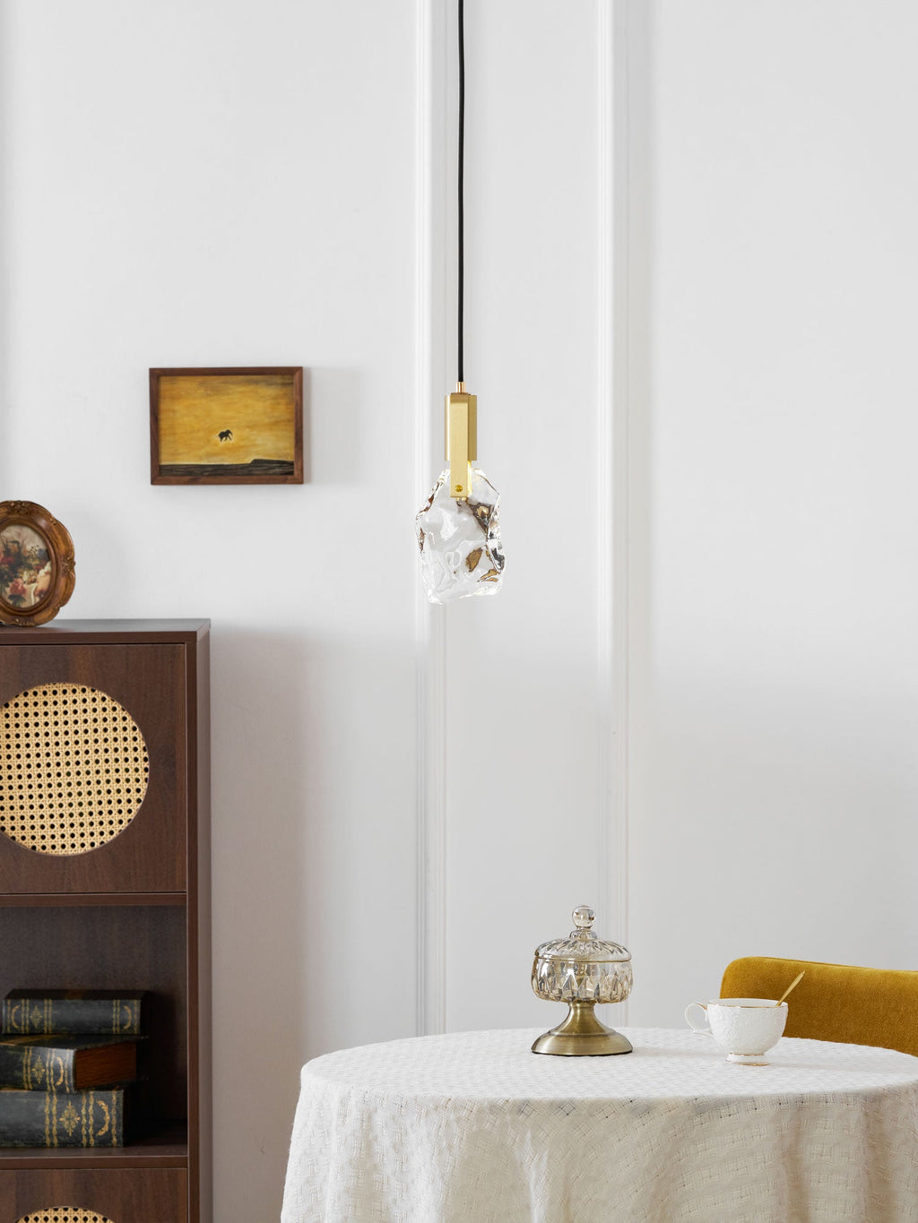A distant view of the rock-glass Clérachic pendant above a round table with a glass jar, with a cane cabinet at the left.