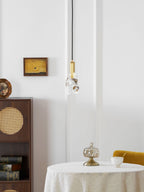 A distant view of the rock-glass Clérachic pendant above a round table with a glass jar, with a cane cabinet at the left.