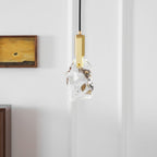 A close view of the rock-glass Clérachic pendant with a brass bracket and a small framed painting on a white wall.