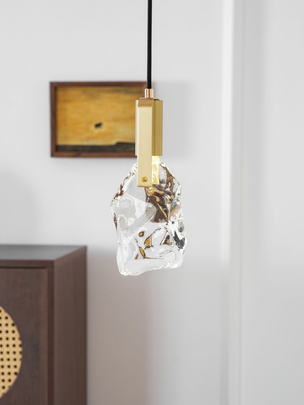 The rock-glass Clérachic pendant seen against a white panelled wall, with a wooden cabinet partly visible at the left.