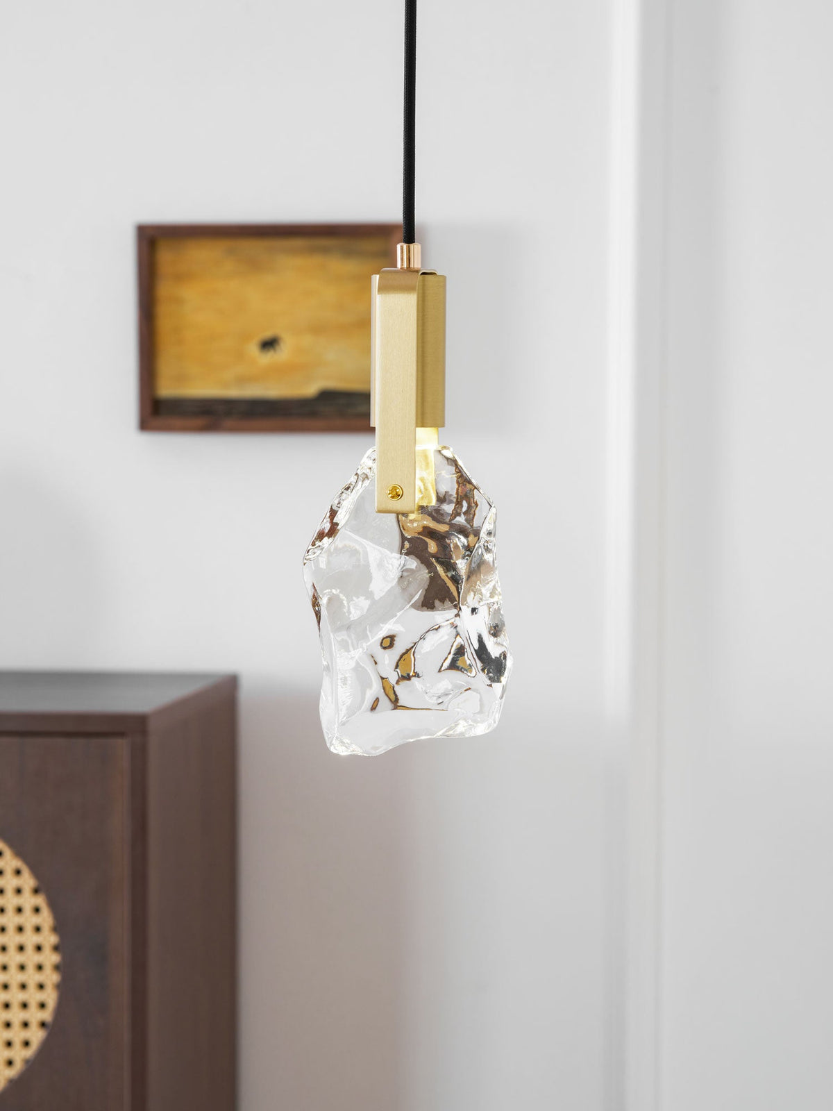 The rock-glass Clérachic pendant seen against a white panelled wall, with a wooden cabinet partly visible at the left.