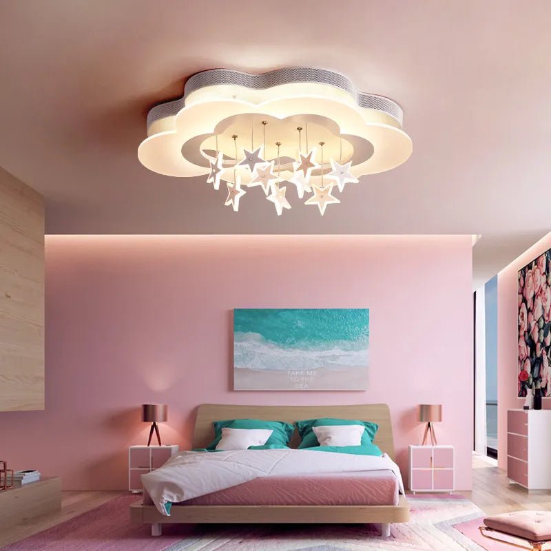 Clérachic cloud-shaped ceiling light with hanging stars glowing above a bed in a pink child's bedroom with a sea print.