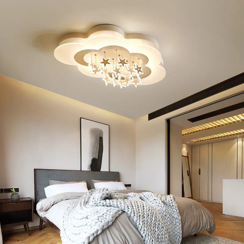 Clérachic cloud-shaped flush ceiling light with a cluster of hanging white stars, lit warm above a bed in a calm room.