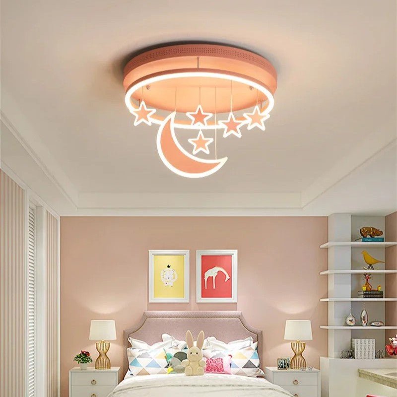 Clérachic round pink ceiling light with a glowing crescent moon and hanging stars above a bed in a soft pink child's room.