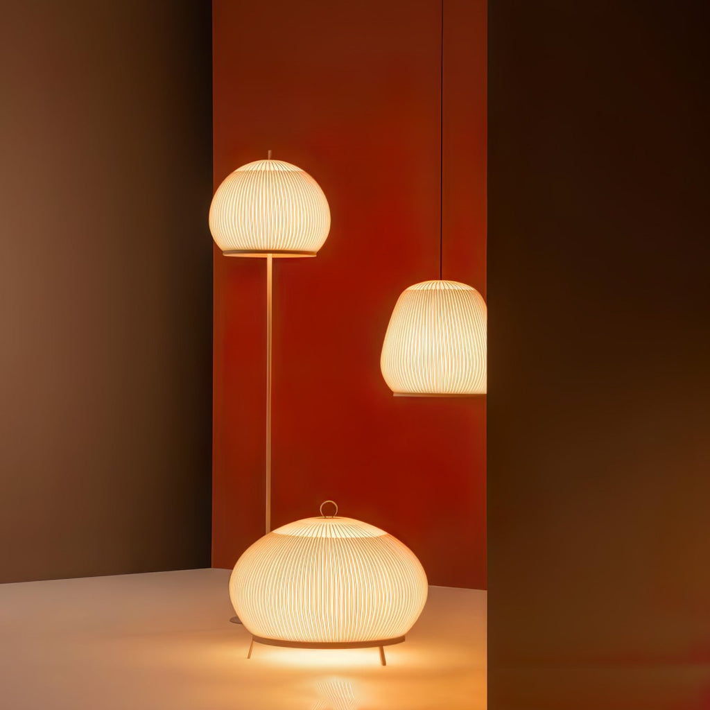 Clérachic knit shades lit together against a deep red wall — a floor lamp, a pendant, and a table lamp on slim tripod feet.