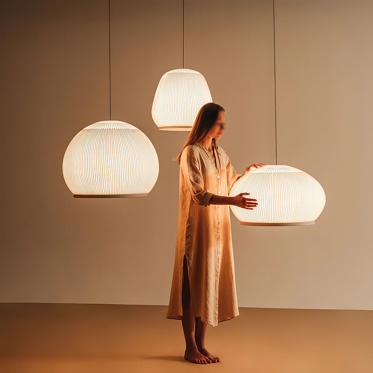 Clérachic knit pendant lamps shown for scale, a woman standing among three lit shades with her hand at the wide dome.