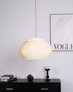 Clérachic wide dome knit pendant lamp lit warm above a black sideboard set with a rounded vase, books, and a tall candlestick.