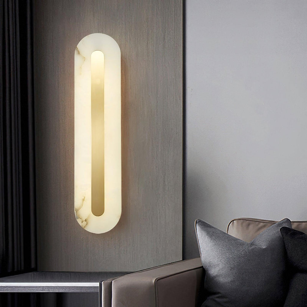 Clérachic Kristy wall lamp lit on grey beside a leather sofa and dark cushions.