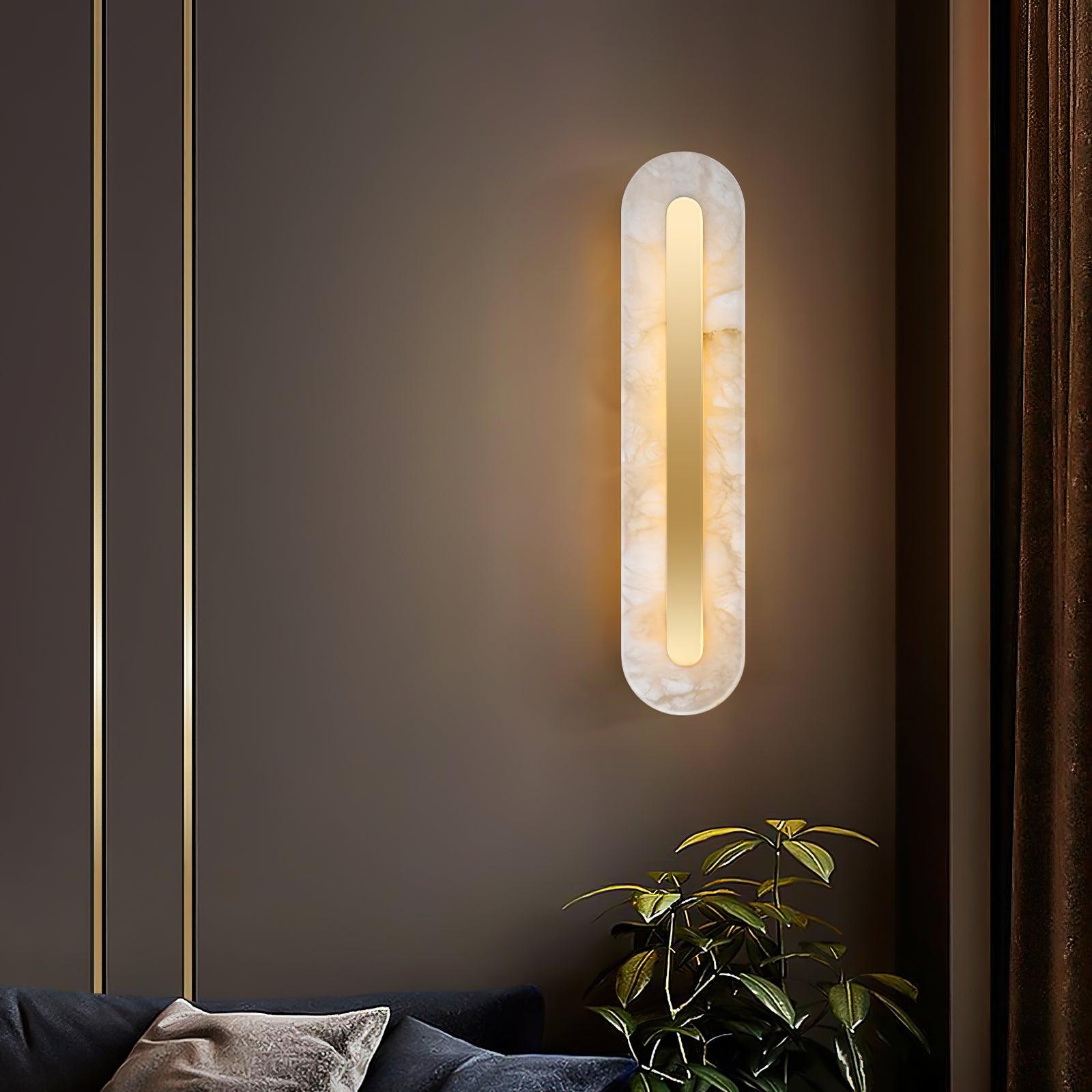 The Clérachic Kristy wall lamp on a dark wall with gold trim, plant leaves beside it.