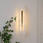 Clérachic Kristy wall lamp lit on cream plaster with green foliage trailing nearby.