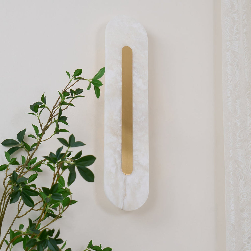 Clérachic Kristy wall lamp angled on cream, foliage and a curtain edge in the frame.