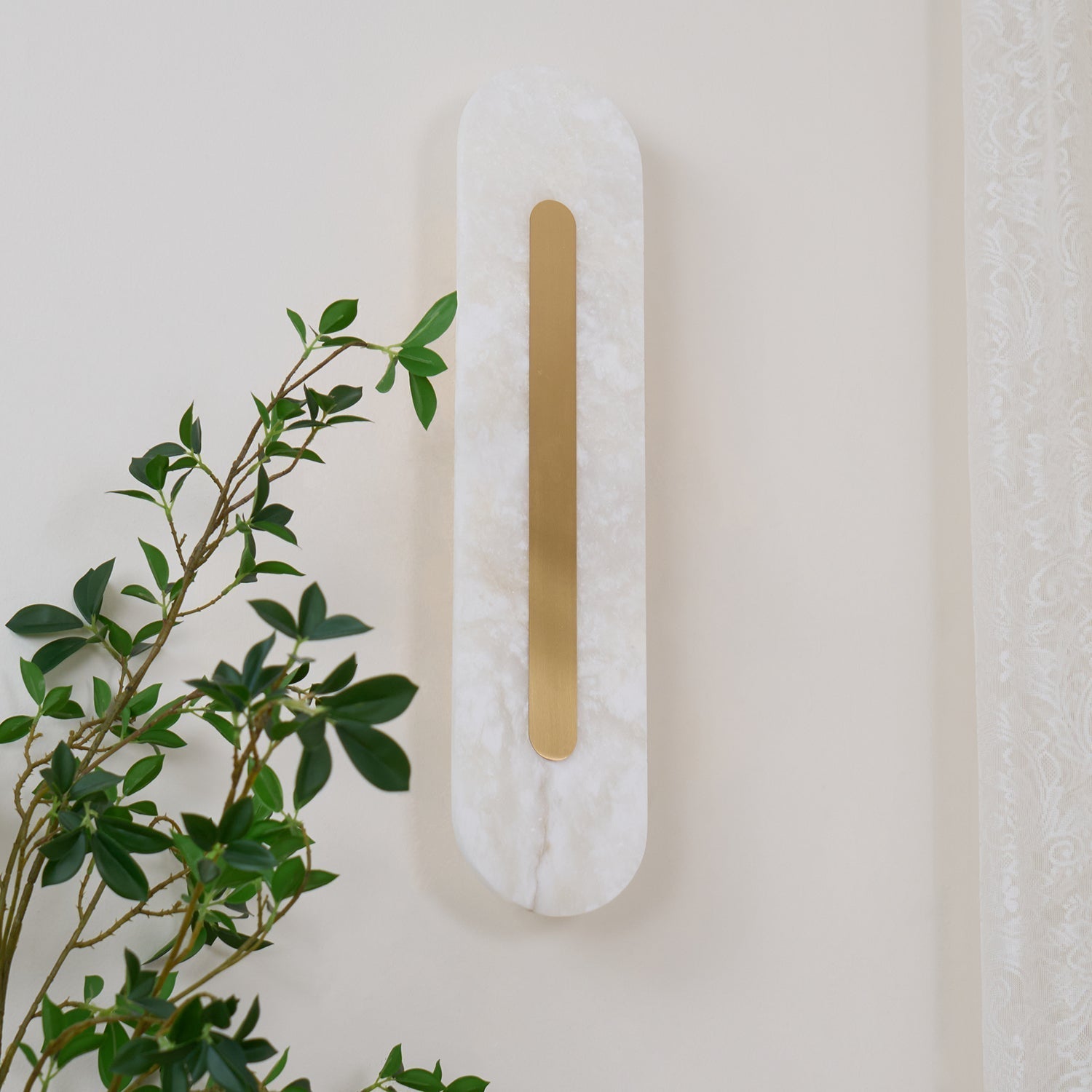 Clérachic Kristy wall lamp angled on cream, foliage and a curtain edge in the frame.