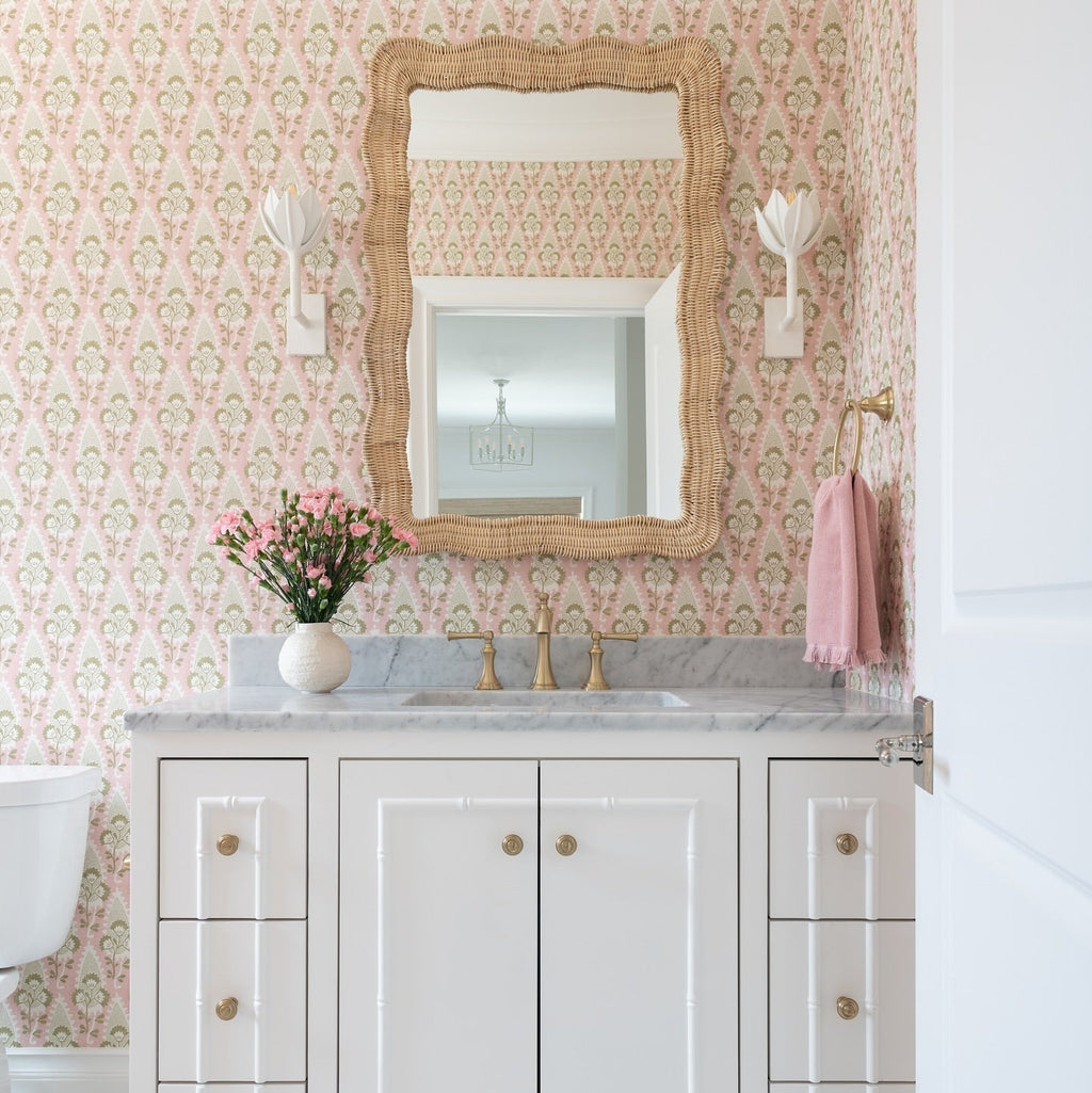 A Clérachic white tulip sconce lights a rattan-framed mirror beside a pink towel in this floral bath.