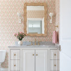 A Clérachic white tulip sconce lights a rattan-framed mirror beside a pink towel in this floral bath.