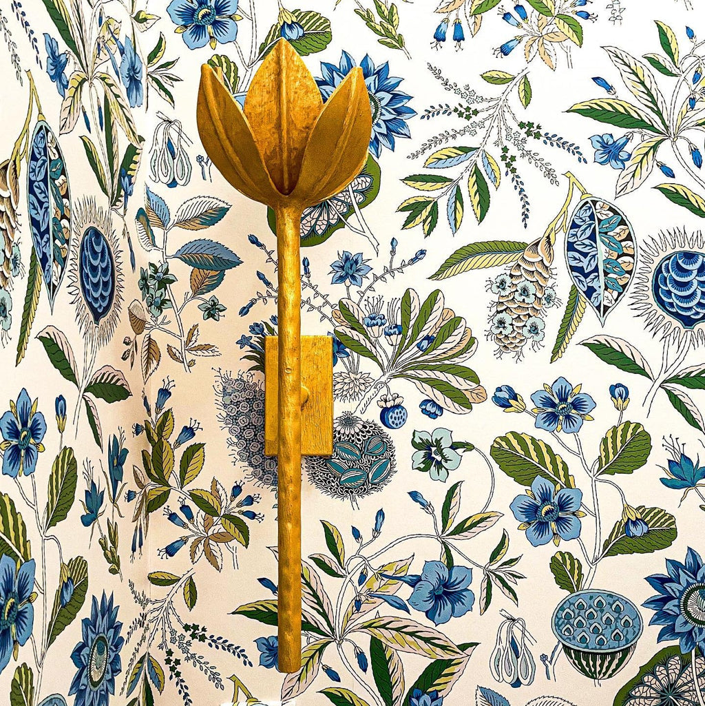 The Clérachic brass tulip sconce sits on a wood mounting block against blue floral wallpaper.