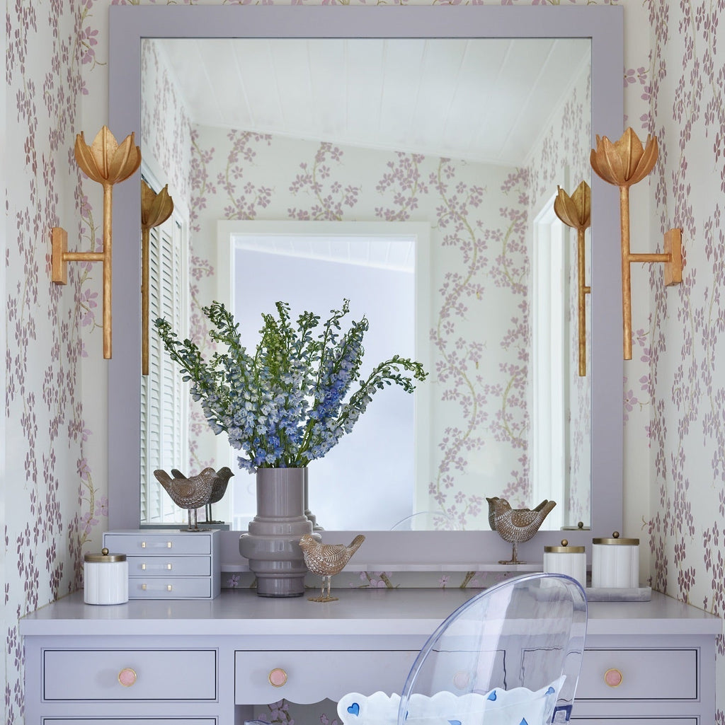 Clérachic sconces flank a lavender mirror above a vanity styled with fresh flowers and small birds.