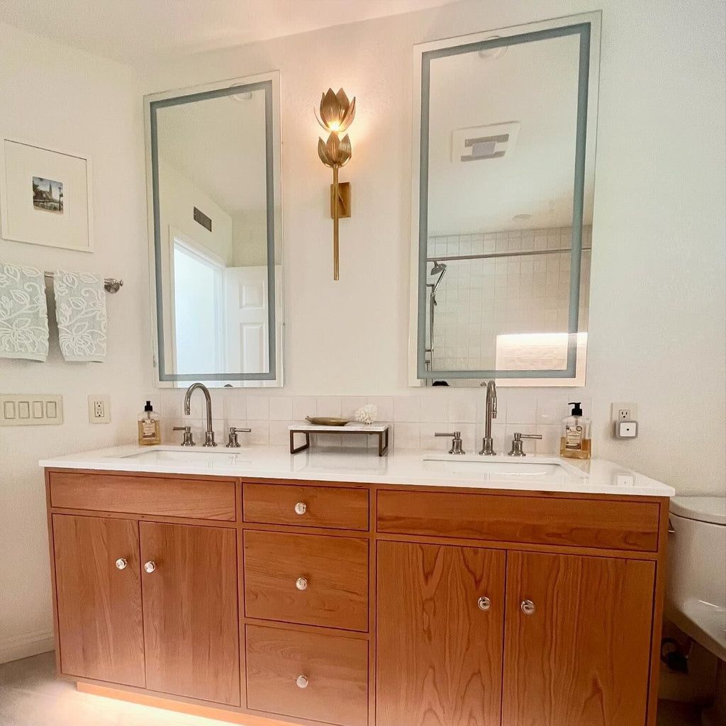 The Clérachic sconce lights a double vanity between two mirrors in a warm wood-cabinet bathroom.