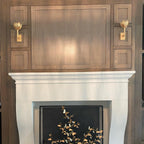 Clérachic brass sconces flank a stone fireplace mantel framed in wood paneling.