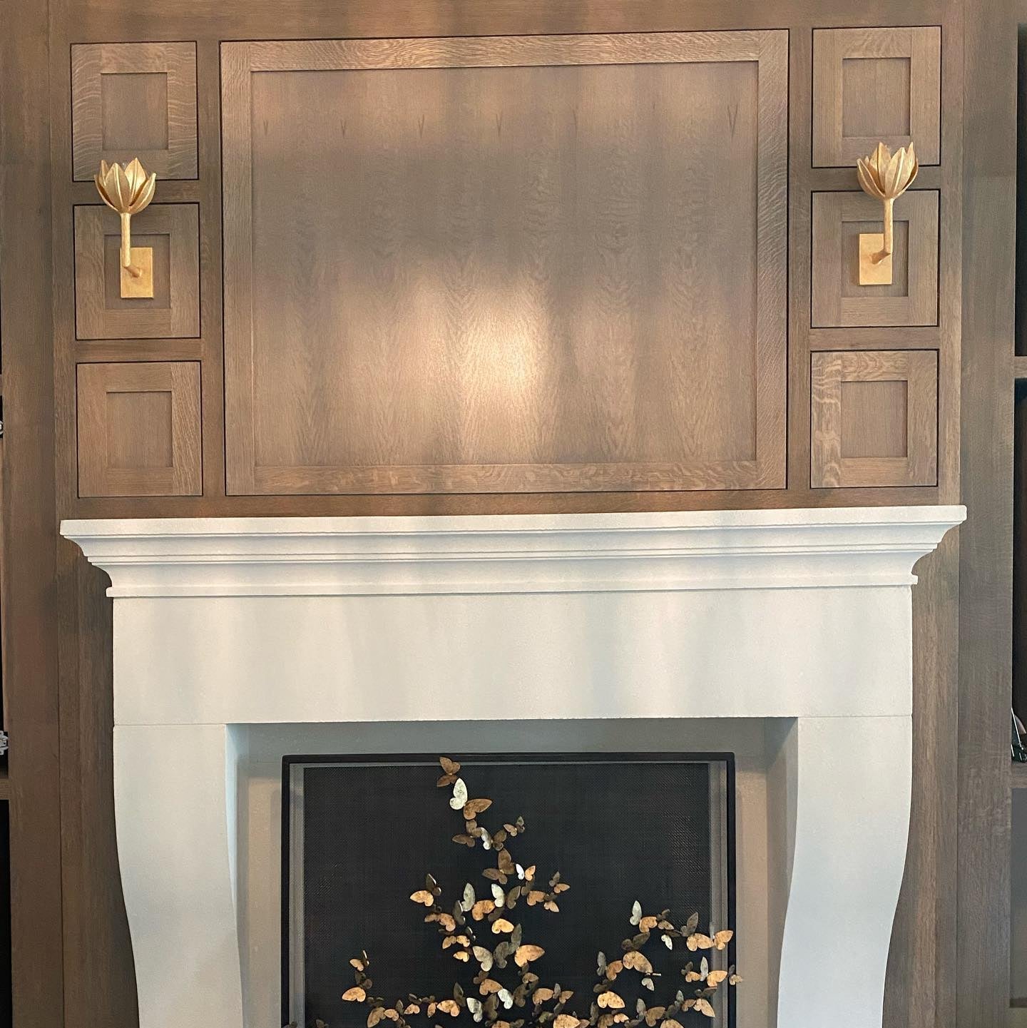 Clérachic brass sconces flank a stone fireplace mantel framed in wood paneling.