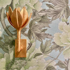 The Clérachic brass tulip sconce mounts on a wood block against green and blush floral fabric.
