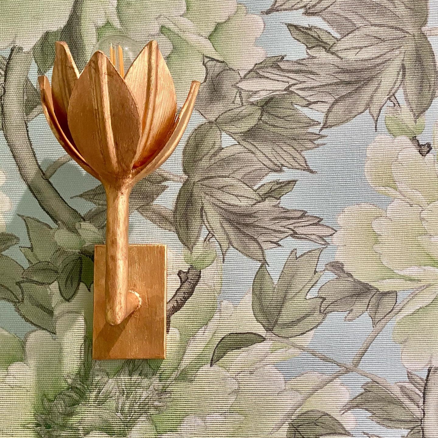 The Clérachic brass tulip sconce mounts on a wood block against green and blush floral fabric.