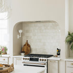 A Clérachic white tulip sconce sits beside an arched tile backsplash over a kitchen range.