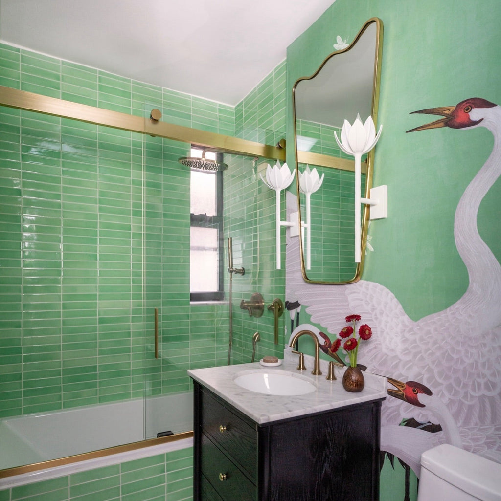 The Clérachic white tulip sconces flank a mirror in a green-tiled bath with a crane-print mural.