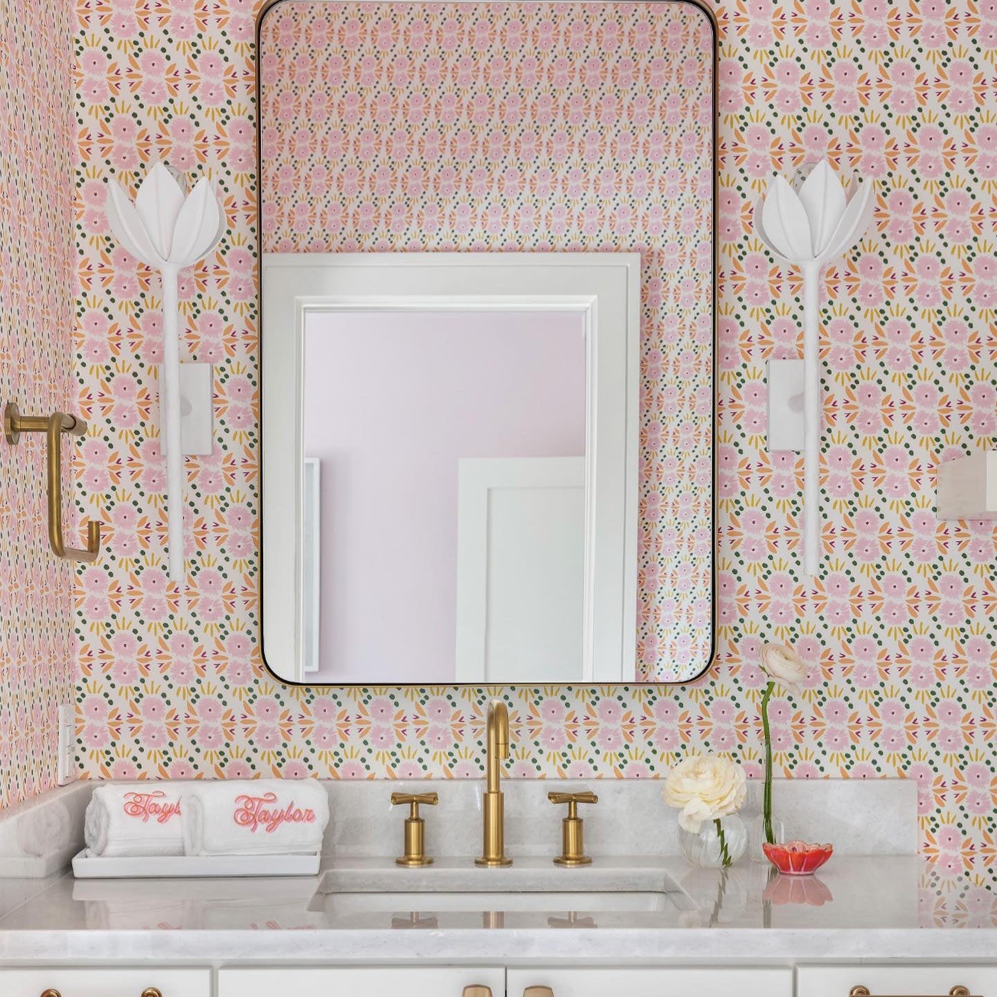 The Clérachic white tulip sconces flank a mirror above monogrammed towels and a brass faucet.