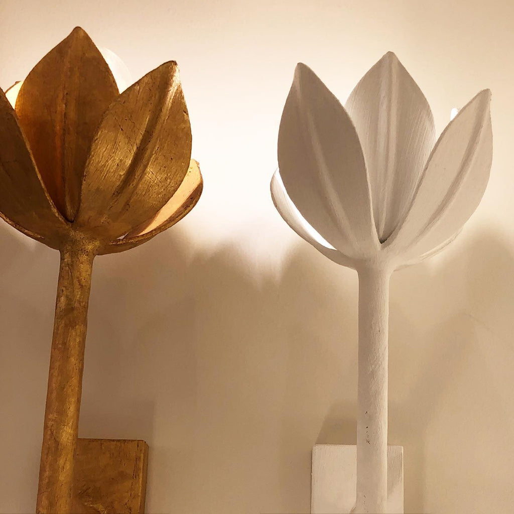 Clérachic tulip sconces stand side by side, one in brass and one in plaster white, on a wood shelf.