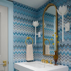 Clérachic white tulip sconces line an arched mirror in a blue chevron-papered bathroom.