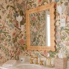 The Clérachic white tulip sconces flank a rattan mirror in a warm floral wallpapered bathroom.