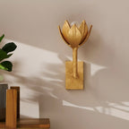A Clérachic brass tulip sconce mounts on a soft pink wall beside a leafy potted plant.