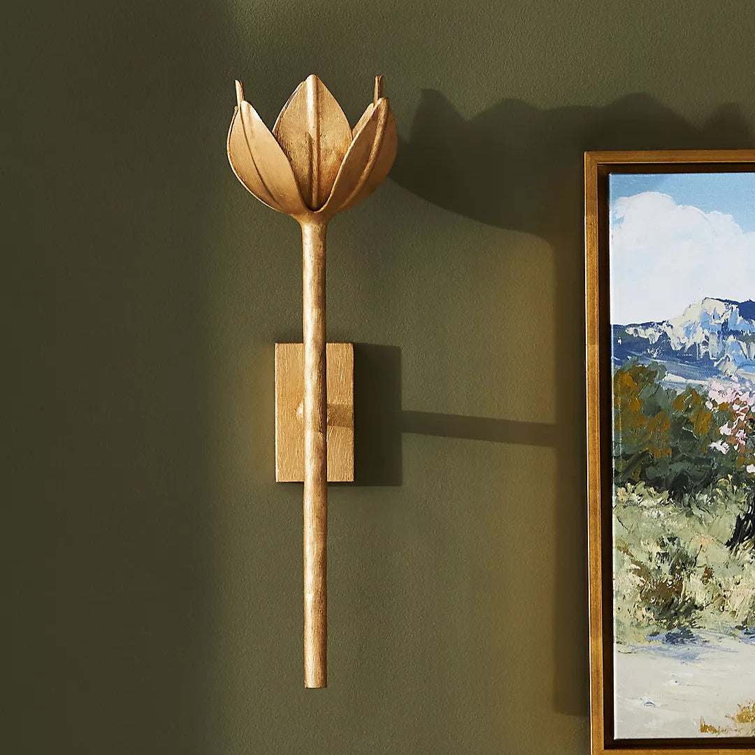 The Clérachic brass tulip sconce lights an olive green wall beside a framed landscape painting.