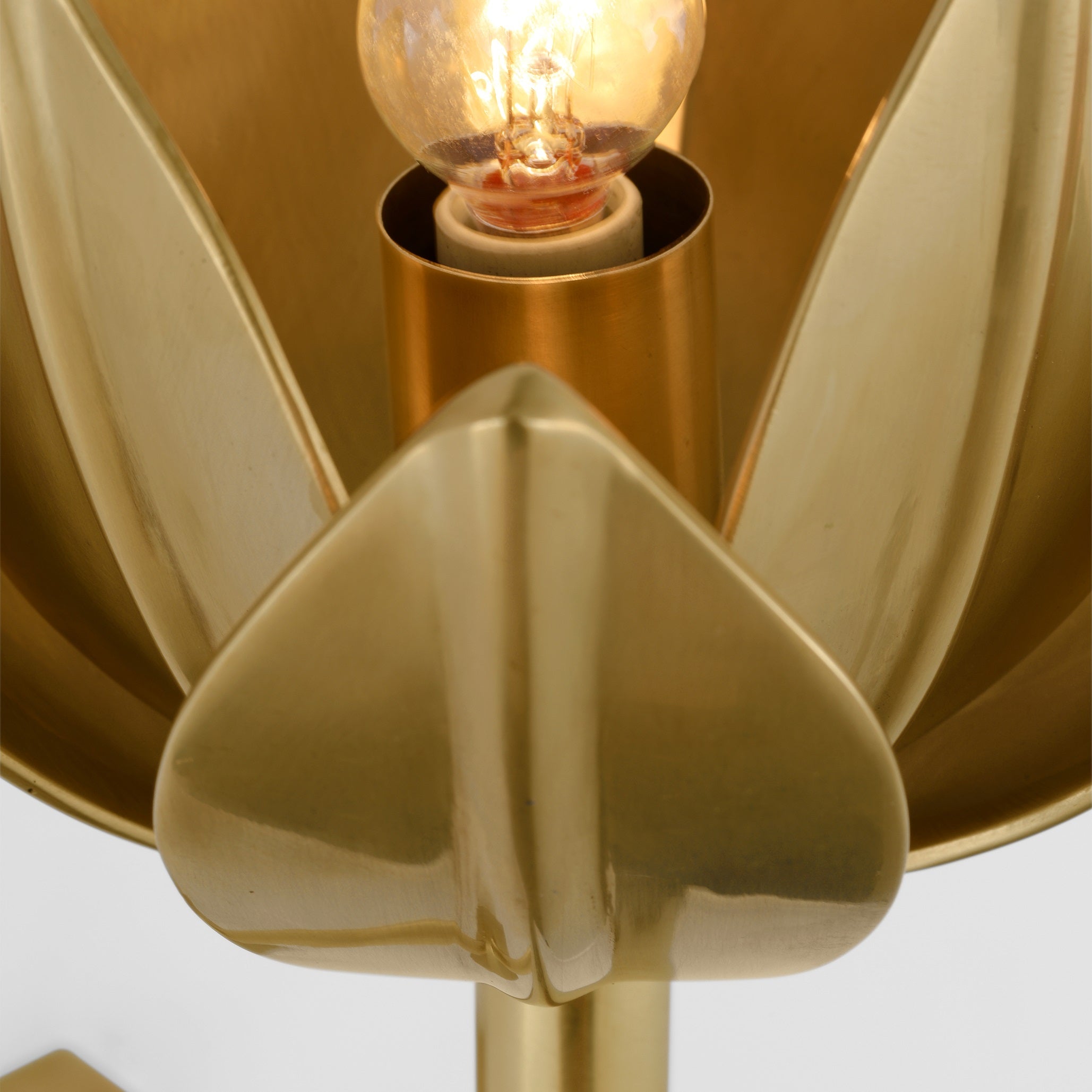 The Clérachic sconce shows its glowing filament bulb seated inside brass petal walls.