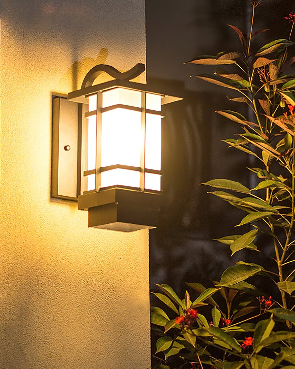 A glowing Clérachic lantern wall light on a cream wall beside a leafy shrub with red berries.