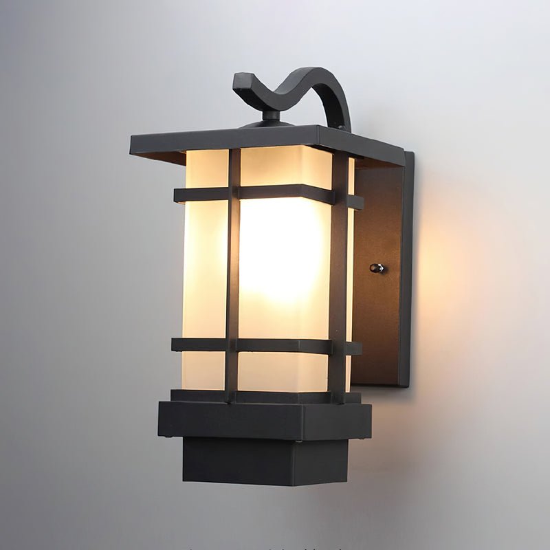 Clérachic black lantern wall light, lit, against a pale grey wall, a curved hook above a banded frosted glass shade.