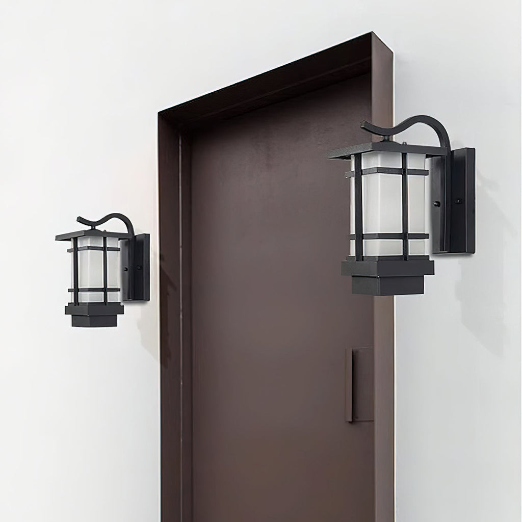 Two Clérachic lantern wall lights flank a dark brown door on a white wall, one smaller than the other, both unlit.