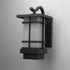 Wall-mounted Clérachic lantern in black aluminium, shown close up against a grey wall, its frosted glass in a grid frame.