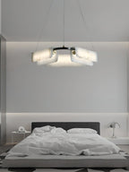 Clérachic Layered Alabaster Plate Chandelier above a low platform bed, glowing softly in a pale grey bedroom.