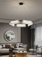 The Clérachic Layered Alabaster Plate Chandelier lit in a living room beside a round landscape panel and pale sofa.
