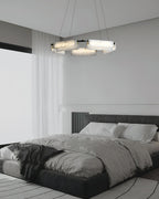 The Clérachic Layered Alabaster Plate Chandelier above a low black bed, soft light spilling across linen bedding.