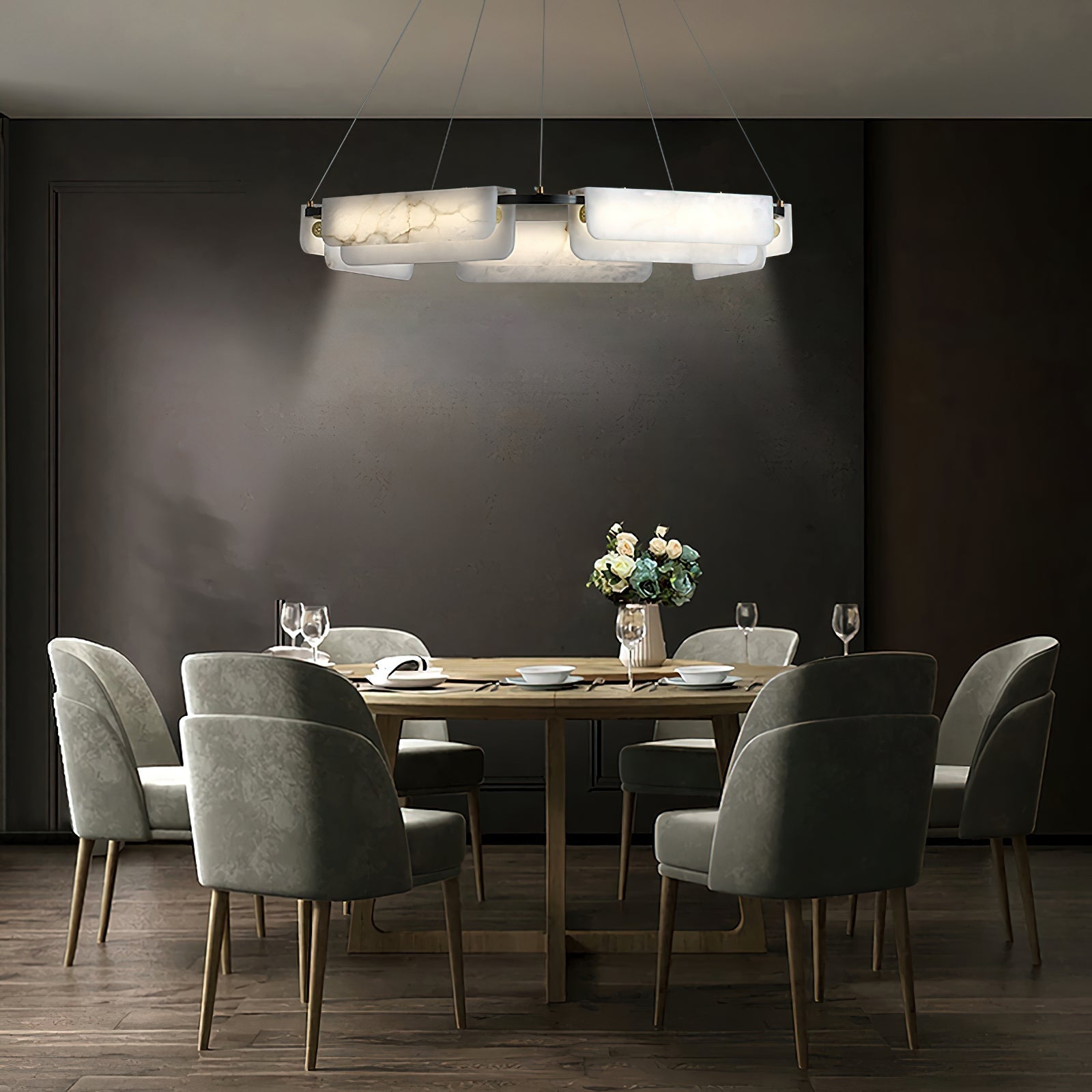 Clérachic Layered Alabaster Plate Chandelier lighting a round dining table and green velvet chairs in a dark room.