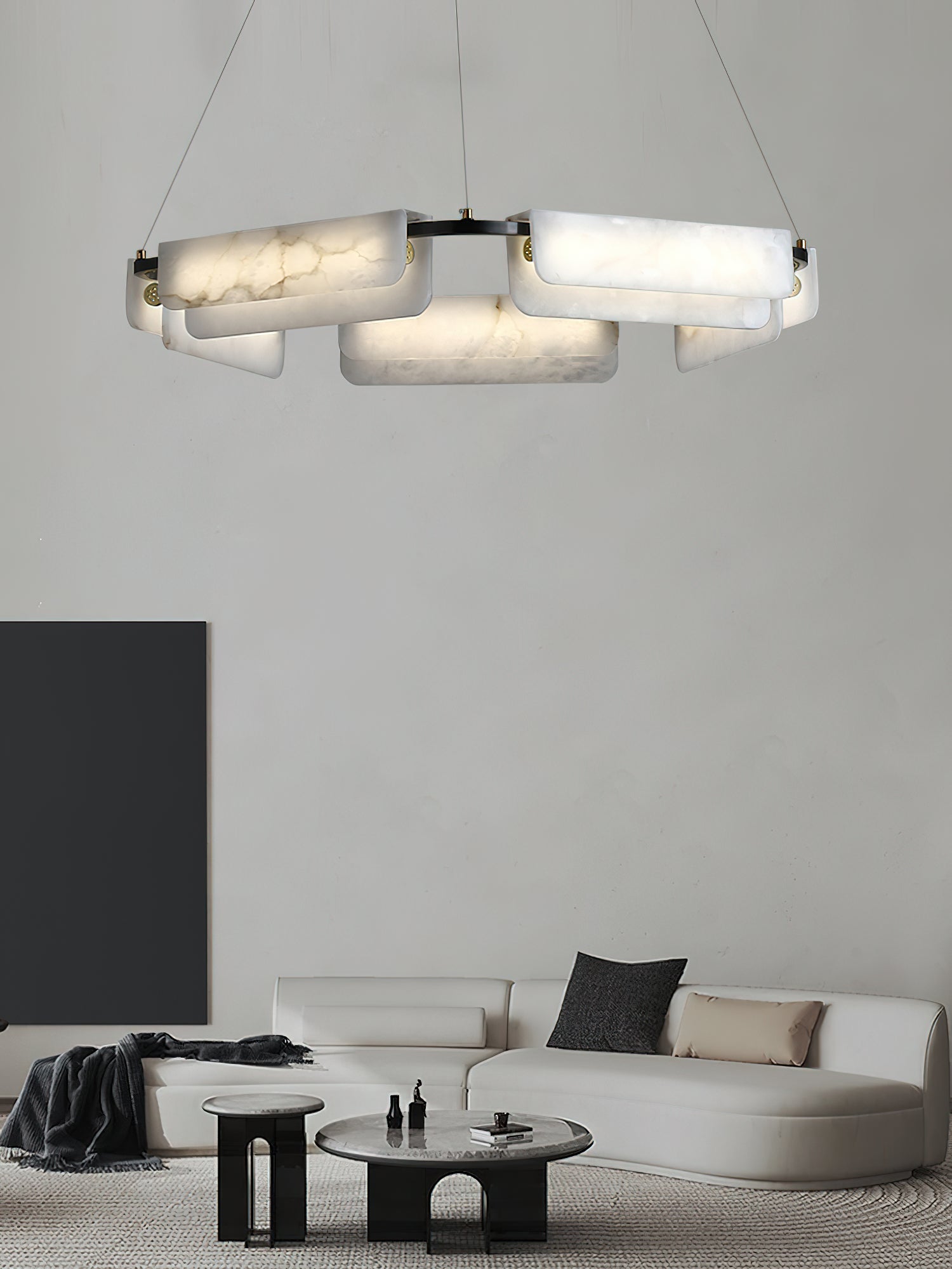 Clérachic Layered Alabaster Plate Chandelier glowing above a curved white sofa in a calm, pale-walled living room.